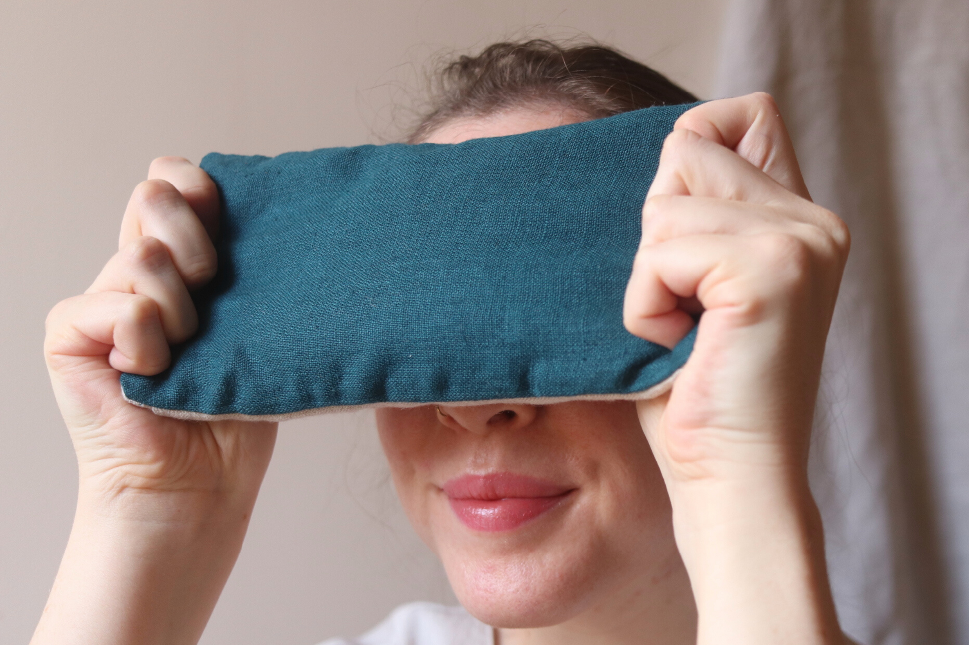 Woman holds blue eye pillow over eyes