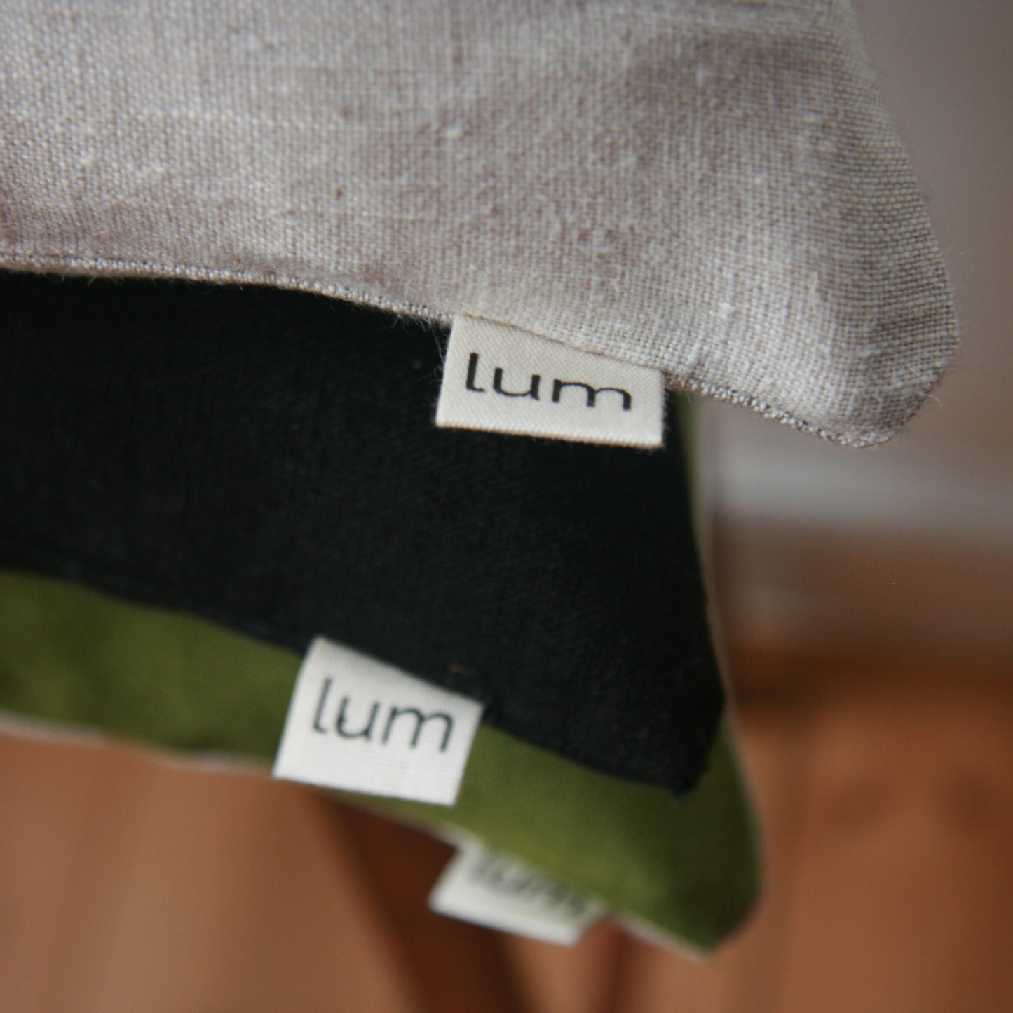 Stack of cushions bearing the logo 'lum'. Green, black and natural linen colours.