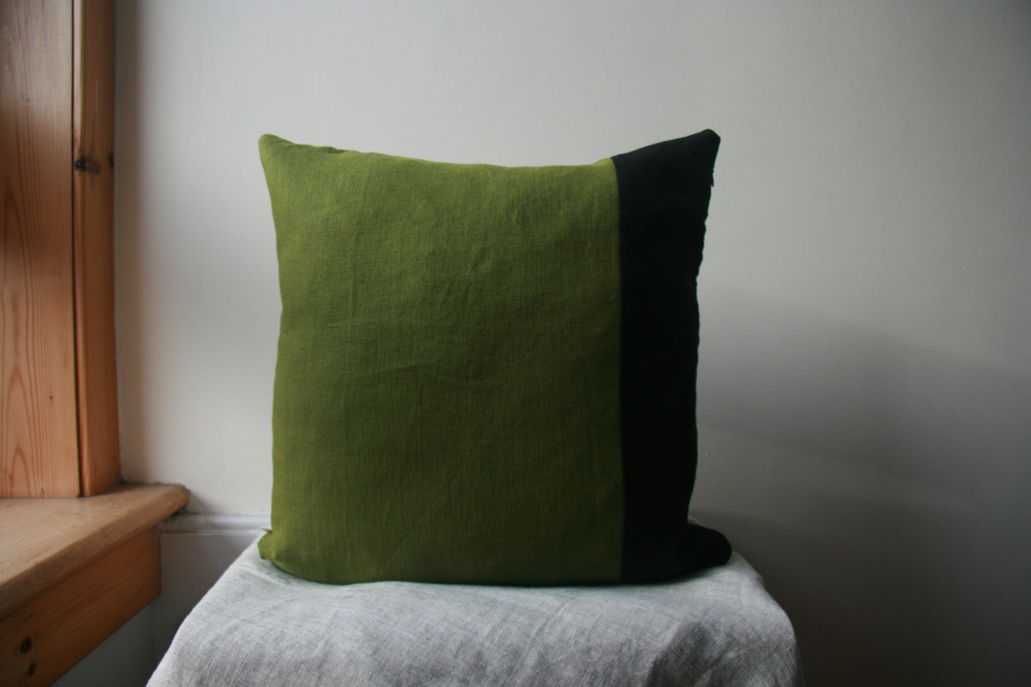 Square cushion cover, of which three quarters is green and one quarter is black. 