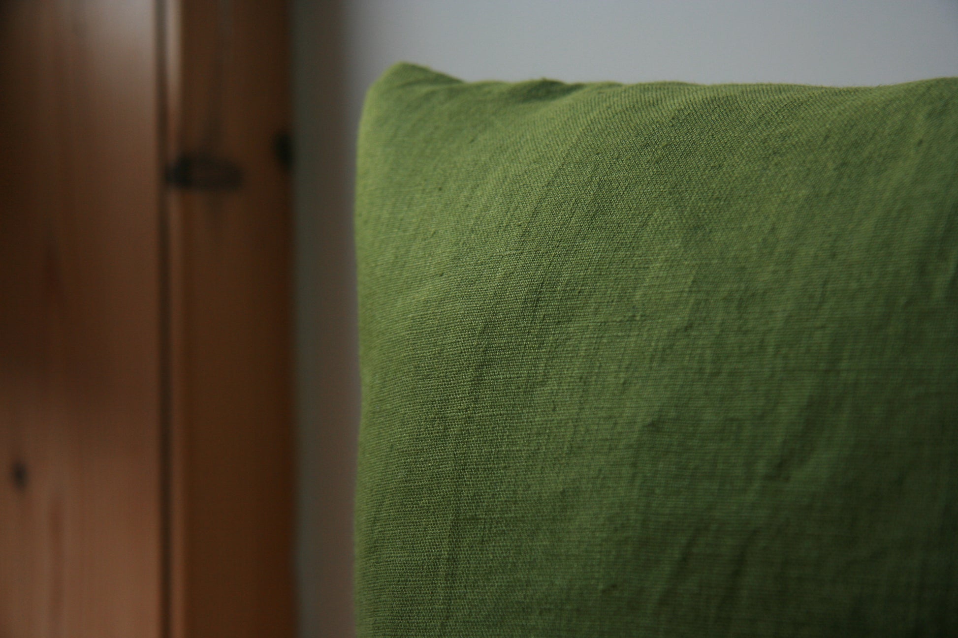 Close up image of corner of cushion. Green fabric visible against background of cream and wood