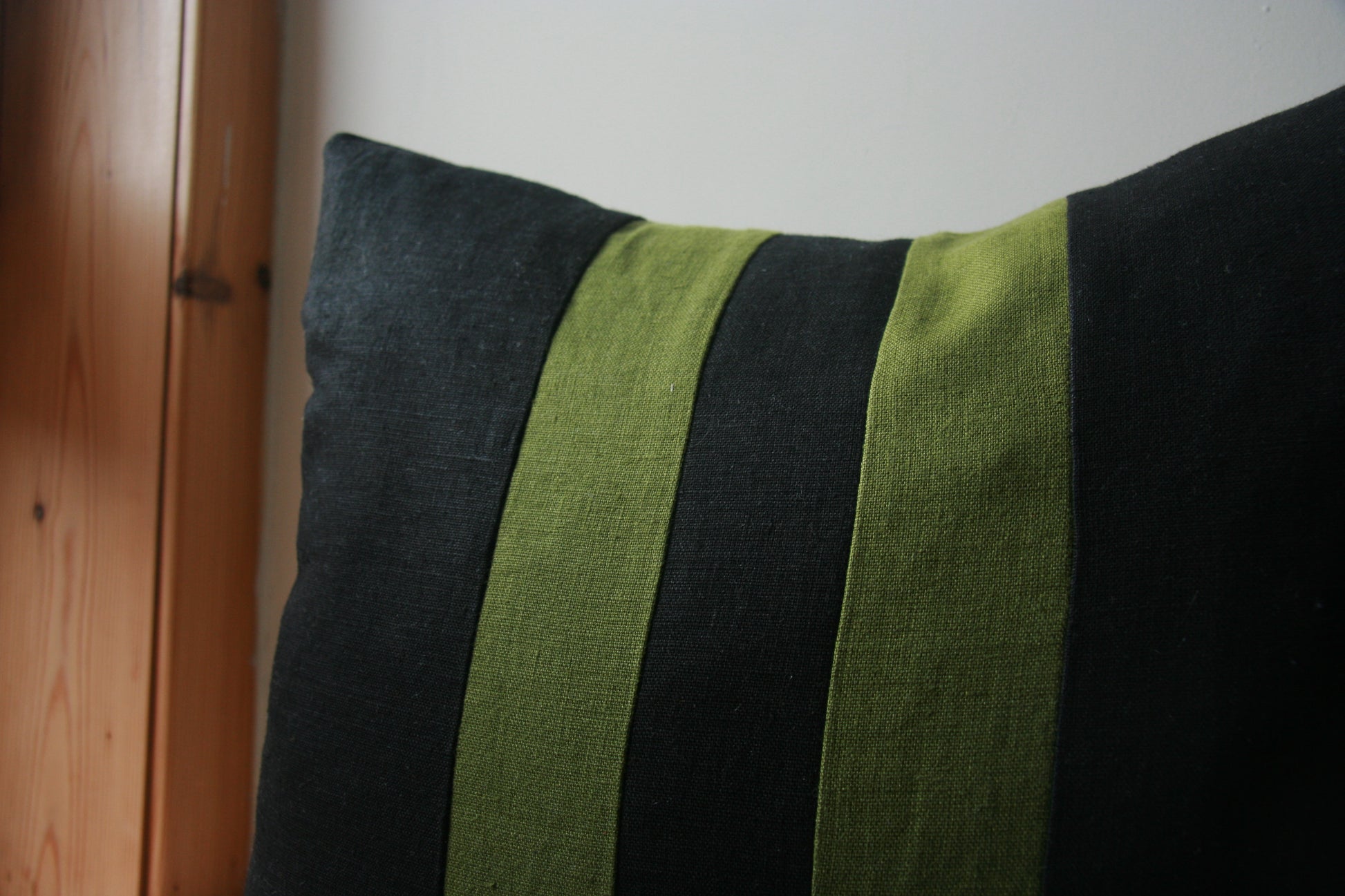 Close up view of corner of cushion cover. Black cushion with parallel green stripes spaced equally from centre