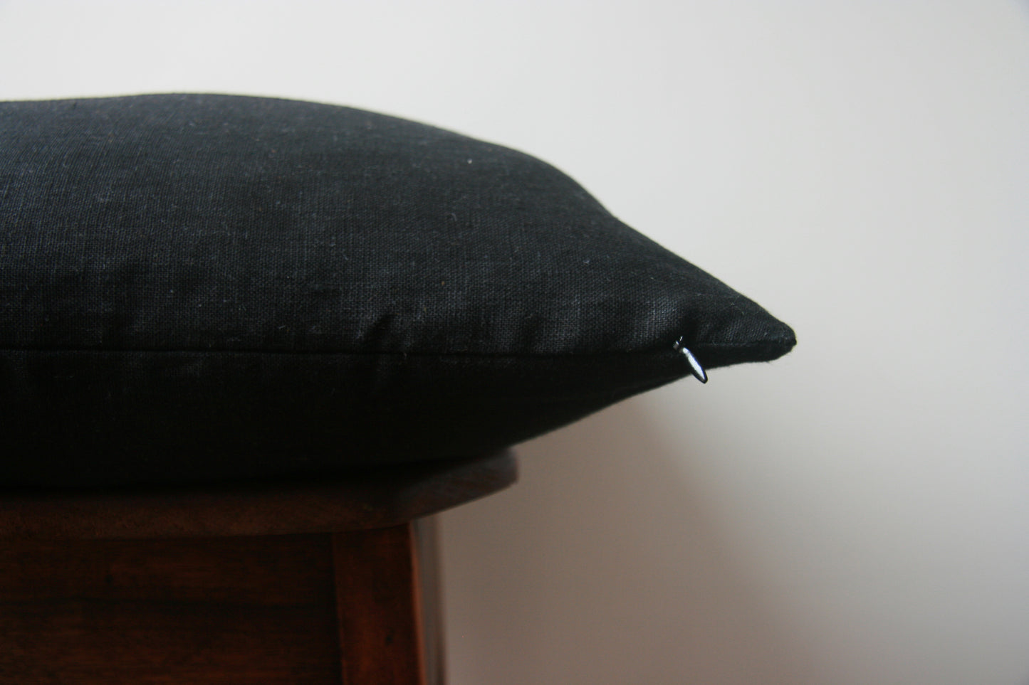Side profile of cushion cover. Black on both sides. Concealed zip with black zipper pull just visible