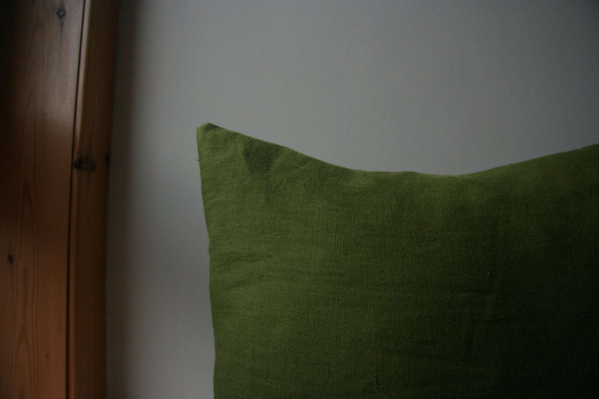 Close up image of corner of cushion. Green fabric visible against background of cream and wood