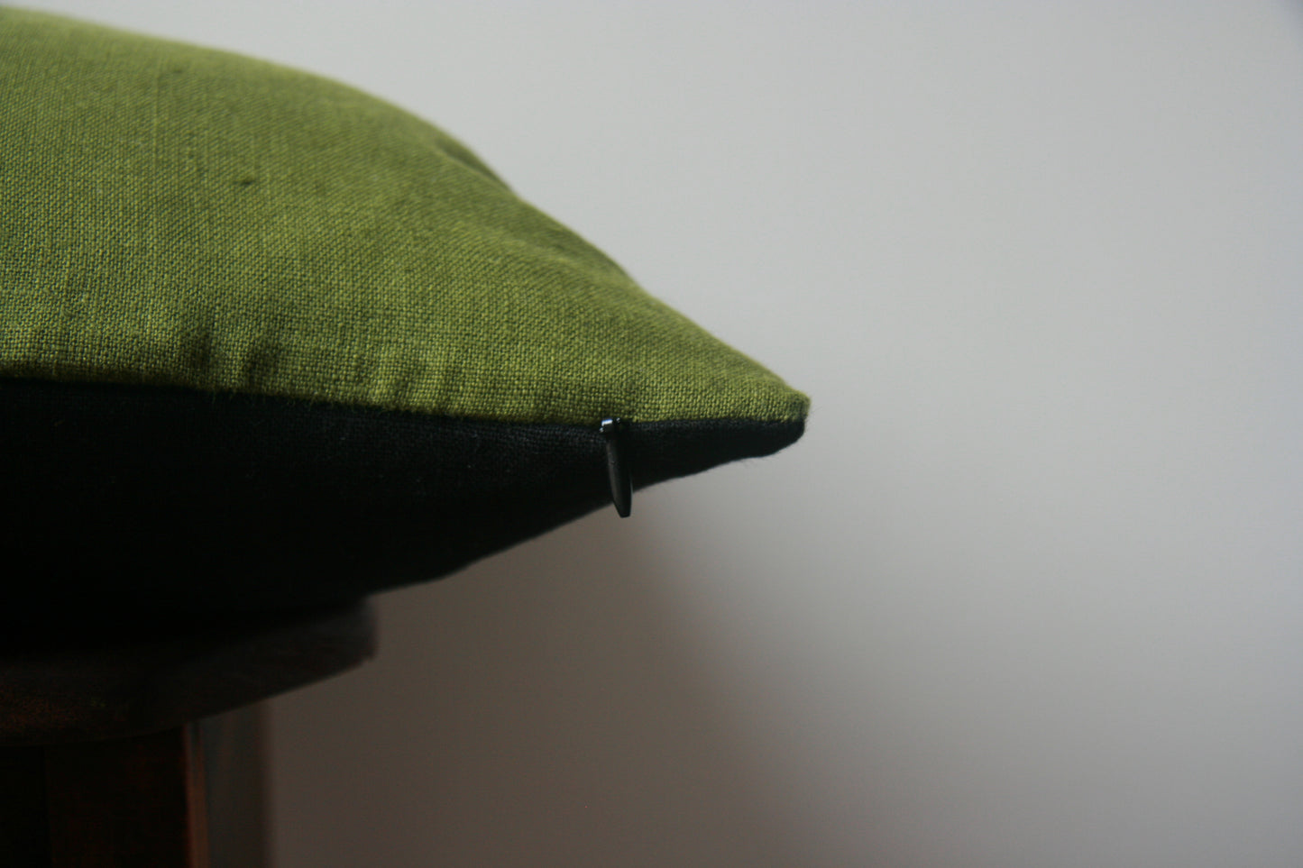 Side profile of cushion cover. Green on top side, black on bottom side. Concealed zip with black zipper pull just visible