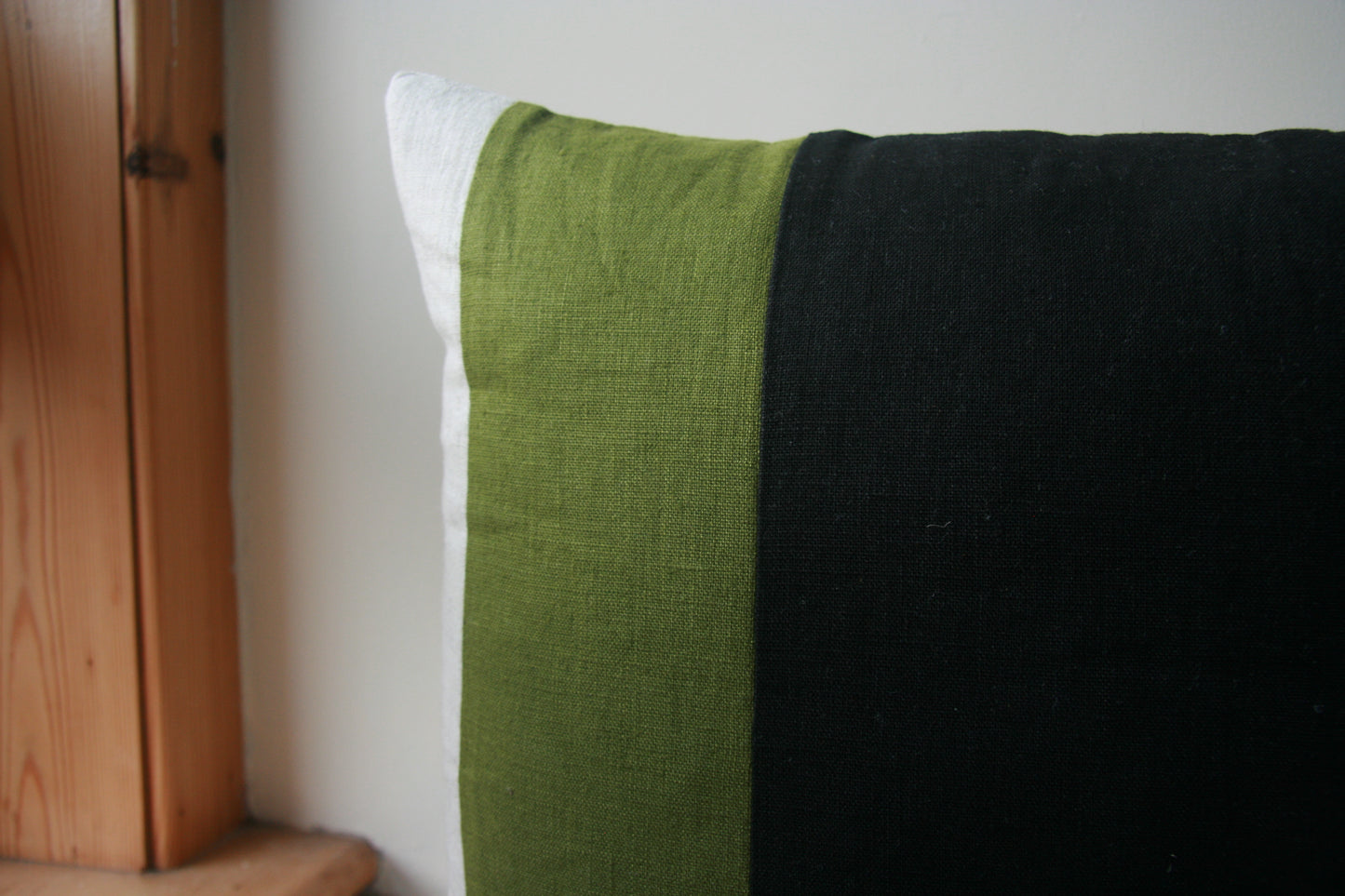 Close up of corner of cushion. Thin natural linen stripe visible, wider green stripe, widest black stripe at edge of image.